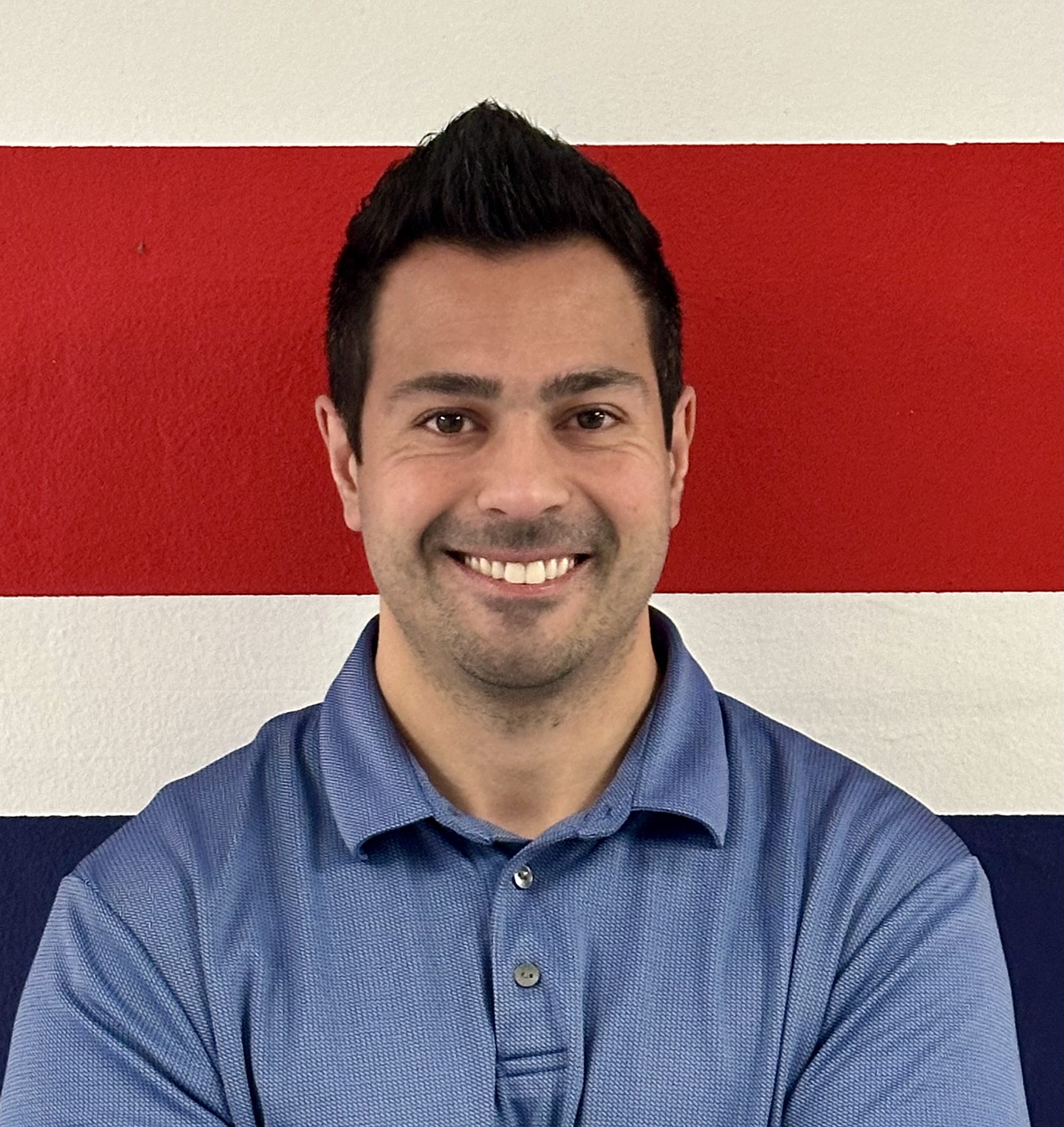 A picture of Gerardo Valenzuela, wearing a blue polo in front a red, white, and blue background